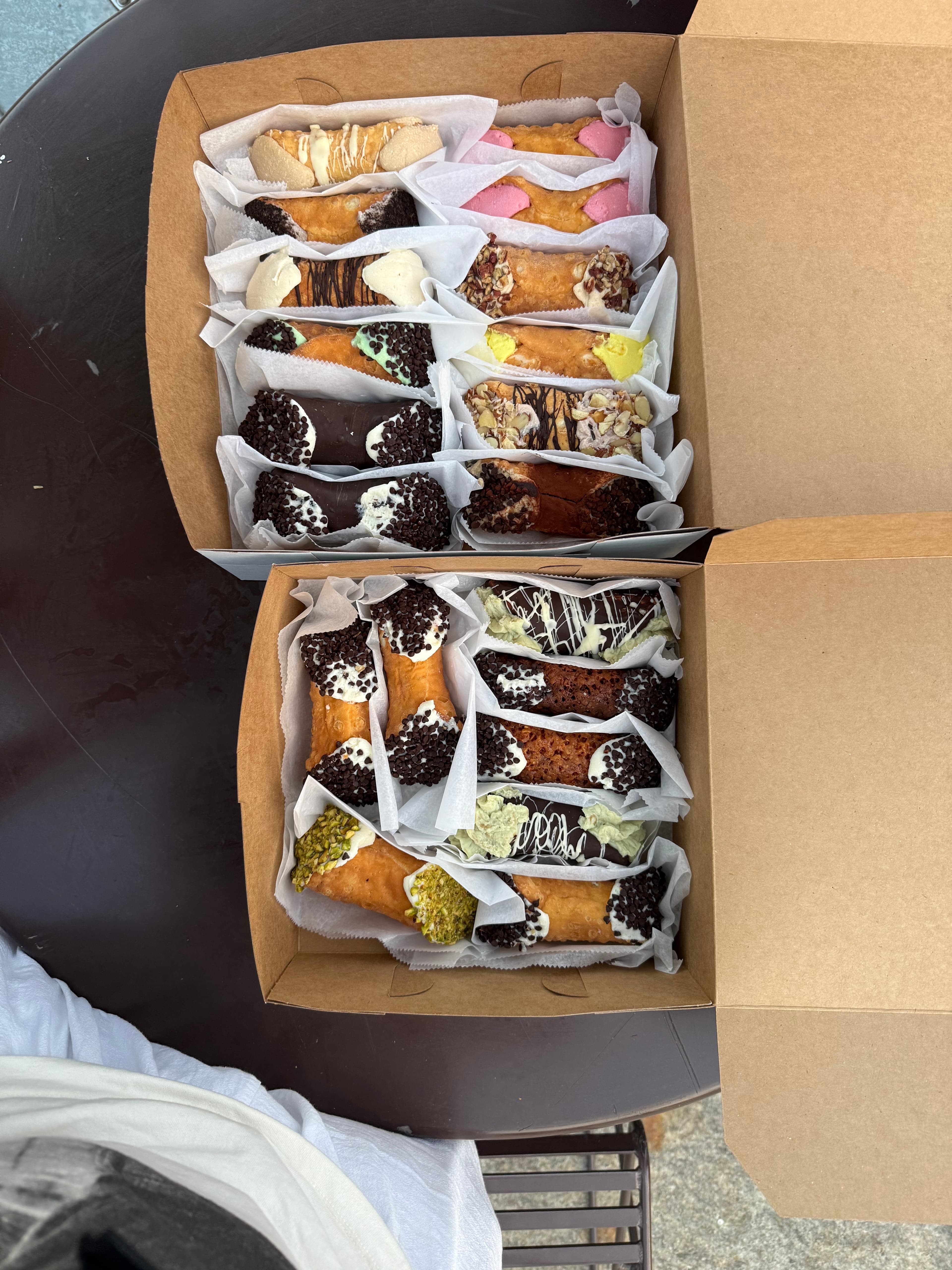 Two open bakery boxes packed with cannoli dipped in chocolate chips, pistachio and cream