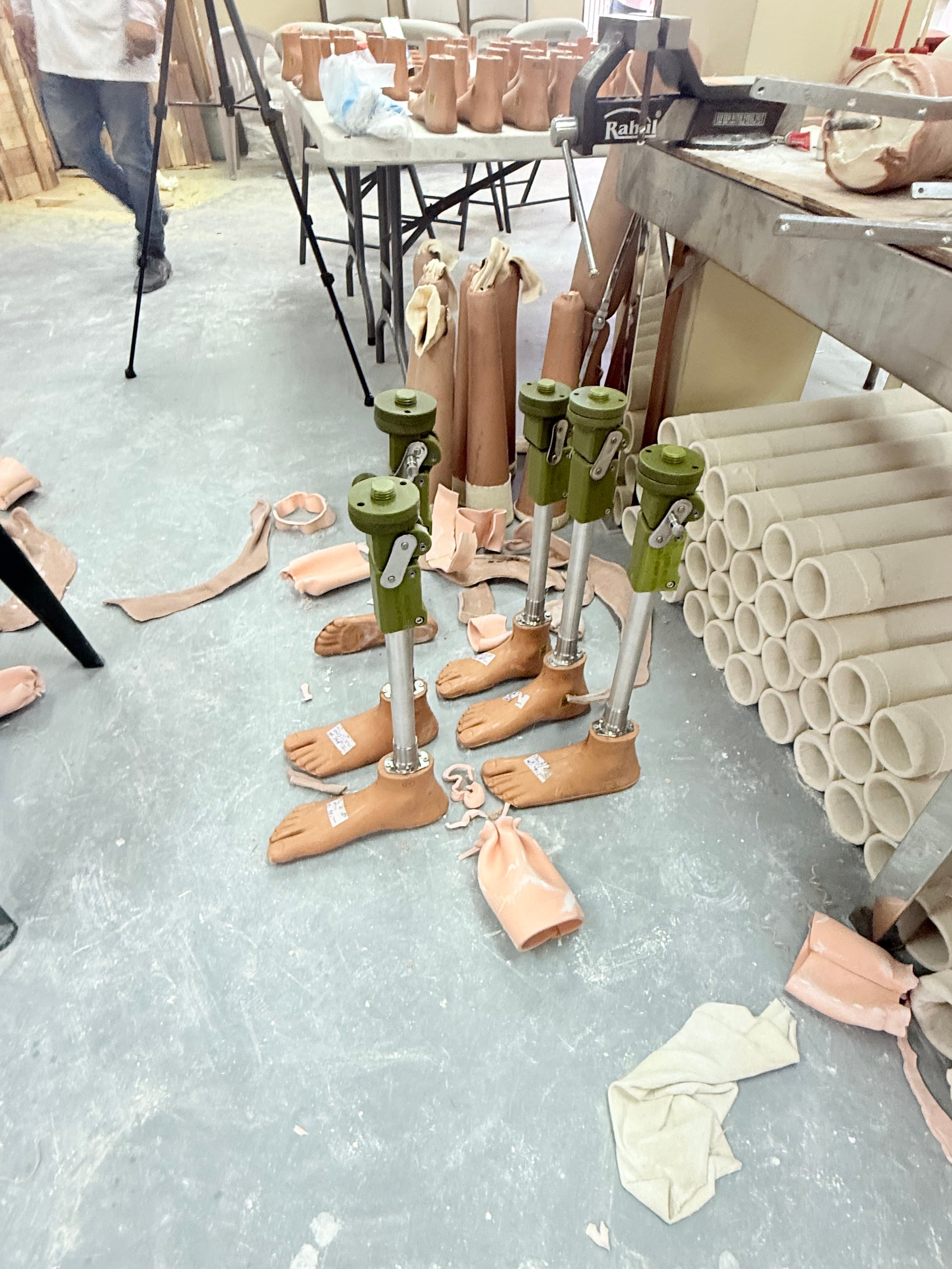 Prosthetic legs and feet laid out on a workshop floor beside stacked casting moulds and clamps