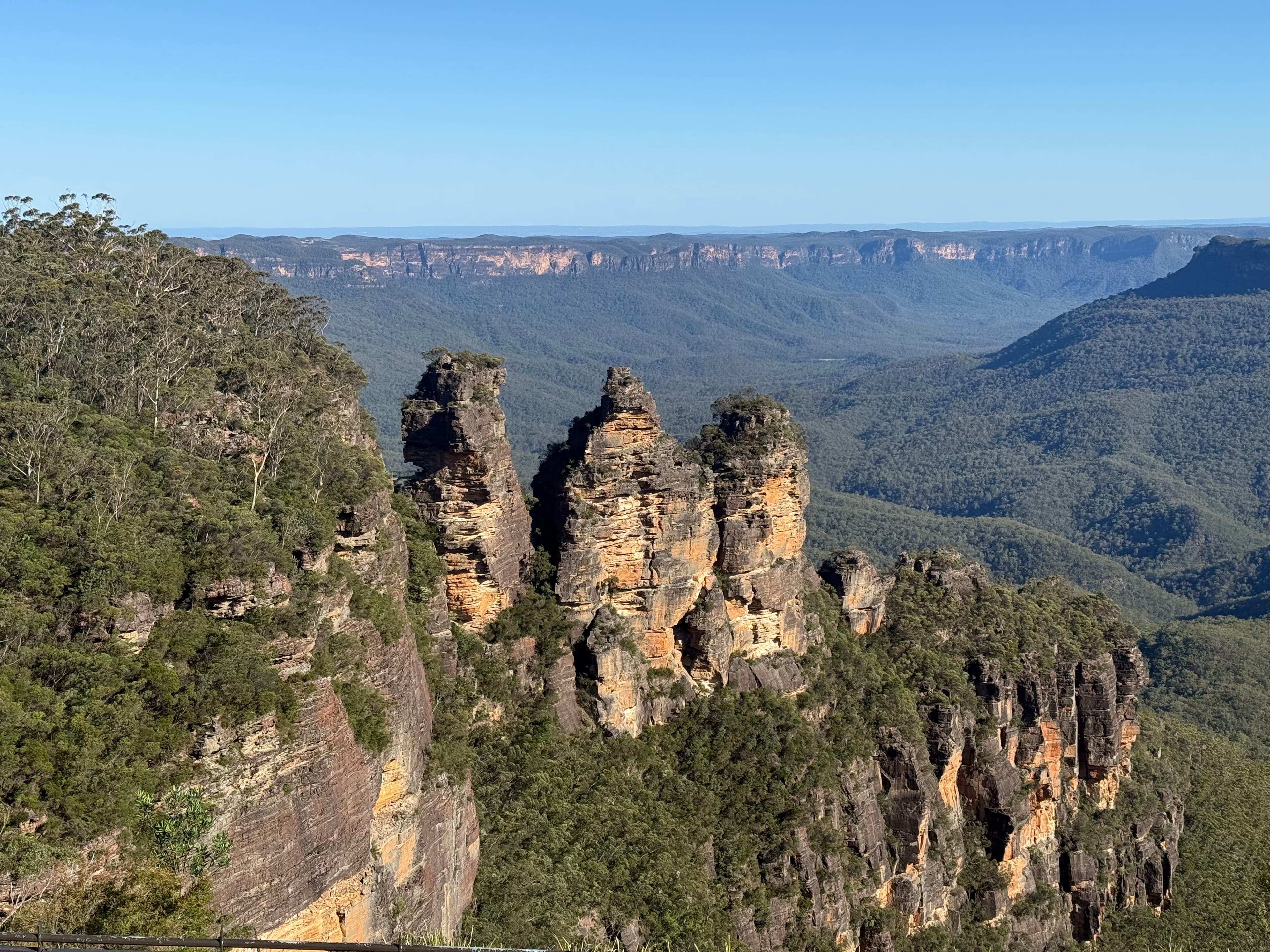 Three sandstone pinnacles on the rim of a forested valley stretching to the horizon