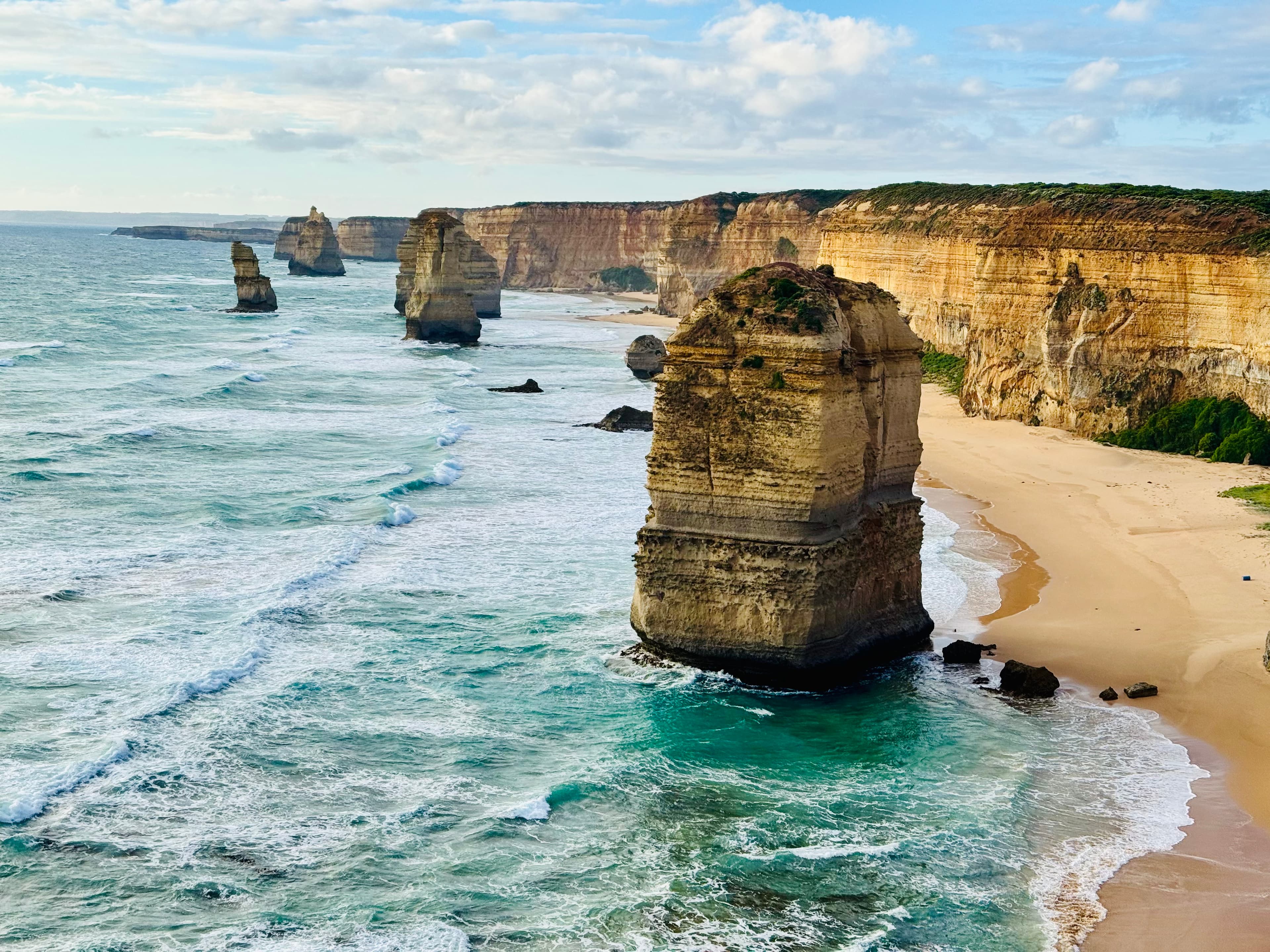 Limestone sea stacks standing off a line of ochre cliffs, surf breaking around them